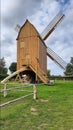 Historic windmill made of light brown wood . Wooden building with barrier band , green grass and very white cloudy sky . Ancient Royalty Free Stock Photo