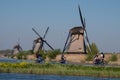 Historic windmills with cyclists cycling along the side of the canal in the foreground, at Kinderdijk, Holland