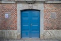 Historical building with old rough brick wall facade, wooden blue shutters of windows and green rough wooden door. Royalty Free Stock Photo