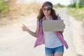 Hitchhiking woman travel. Beautiful young female hitchhiker in a cap and sunglasses smiles and catches a passing car by Royalty Free Stock Photo