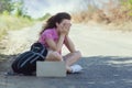 Hitchhiking woman travel. Beautiful young woman with a tourist backpack and a cardboard for text sits near the road and