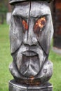 Hitching post on background of ail house. Carved from a log in the shape of a wooden idol`s face