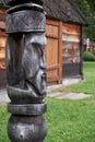 Hitching post on background of ail house. Carved from a log in the shape of a wooden idol`s face