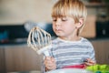 Hmmm...needs more sugar. an adorable little boy licking the batter from a whisk while baking at home.