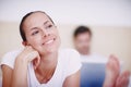 Hmmm, a romantic getaway would be nice...A smiling young woman lying on a bed while her husband works on a laptop in the Royalty Free Stock Photo