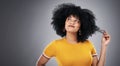 Hmmm what can I do with my hair today. Studio shot of an attractive young woman posing against a grey background.