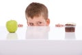 Hmmm...what to do. a mischevious boy peeking over at a table that has a cupcake and an apple on it. Royalty Free Stock Photo