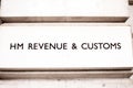 HMRC Sign on a white bricked wall in London. Her Majestys Revenue and Customs collects all taxes and revenue withing reat Britain