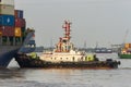 Tugboat Pushing A Large Container Ship To Harbour For Unload.