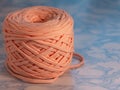 A coil of large knitted yarn of peach color on the surface of blue marble