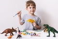 Hobby: a boy, a preschooler, paints with a brush and a tassel a small figure of a dinosaur toy.