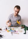 Hobby: a man paints dinosaur toy figures with a brush and paints on a white table Royalty Free Stock Photo