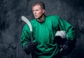 Hockey player holds protective helmet and playing stick on grey