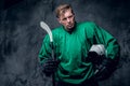 Hockey player holds protective helmet and playing stick on grey