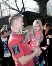 A little girl sitting in her father`s arms laughs because the lemur crawled over her father