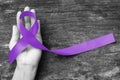 Hodgkin`s lymphoma and testicular cancer awareness violet ribbon symbolic bow color on helping hand support and aged wood