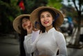 Two beautiful Vietnamese women in traditional Ao Dai dress riding a bicycle Royalty Free Stock Photo