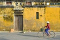 Hoi An / Vietnam, 12/11/2017: Local Vietnamese woman with rice hat on a bicycle passing in front of traditional houses with