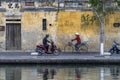 Asian woman rides a bicycle and a man rides a motorbike the road near the river in the old city against the background of the old Royalty Free Stock Photo