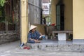 Old vietnamese woman in a straw hat sits on a street near home in the old city in Hoi An, Vietnam Royalty Free Stock Photo