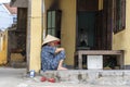 Old vietnamese woman in a straw hat sits on a street near home in the old city in Hoi An, Vietnam Royalty Free Stock Photo