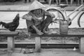 A Vietnamese old woman in a straw hat sits on a bench and eats food on a street in the old city in Hoi An, Vietnam, black and Royalty Free Stock Photo