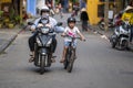 Vietnamese woman with her children rides a motorbike and bike along the road in the Old Town Hoi An, Vietnam