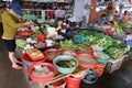 A woman buys vegetables while the shop assistant eats with chopsticks at the Ba Le market in Hoi An