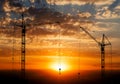 Hoisting cranes working on beautiful cloudy sky with orange sunset