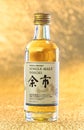 Glass bottle miniature of single malt Yoichi from the Japanese distiller Nikka Whisky on a golden background.