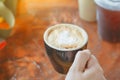 Hold hot coffee, heart shape with milk latte on top of black ceramic cup on hand at coffee shop and cafe in vintage tone, copy Royalty Free Stock Photo