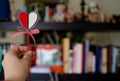 Hold in your hand a decorative heart on a stick. In the background is a dark background. Valentine`s Day