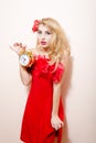 Holding alarm clock beautiful glamour young blond pinup woman in red dress with flower in her hair looking at camera on white