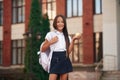 Holding an apple. School girl in uniform is outdoors near the building