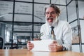 Holding box with tools. Mature businessman with grey hair and beard in formal clothes is in the office