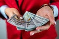 holding cash fans of dollars in hands in white shirt and red jacket isolated on solid color Royalty Free Stock Photo