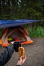 Holding a cup of tea and a croissant in front of an orange tent camping forest Royalty Free Stock Photo