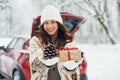 Holding gift box. Beautiful young woman is outdoors near her red automobile at winter time Royalty Free Stock Photo