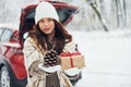 Holding gift box. Beautiful young woman is outdoors near her red automobile at winter time Royalty Free Stock Photo