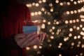 Holding gift box with red bow against blurred Christmas lights Royalty Free Stock Photo