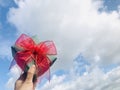 Holding a green gift with a red ribbon against the blue sky and white clouds background. Royalty Free Stock Photo