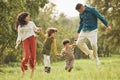 Holding hands, park and parents jump with children in nature for playing, bonding and fun together in field. Happy Royalty Free Stock Photo