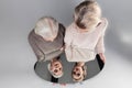 Light-haired curious women in light knitted sweaters glancing in mirror