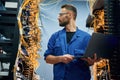 Holding laptop. Young man is working with internet equipment and wires in server room Royalty Free Stock Photo