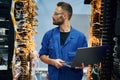 Holding laptop. Young man is working with internet equipment and wires in server room Royalty Free Stock Photo