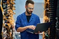 Holding laptop. Young man is working with internet equipment and wires in server room Royalty Free Stock Photo
