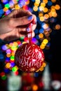 Holding Merry Christmas bauble decoration isolated on background with blurred lights. December season, Christmas composition Royalty Free Stock Photo