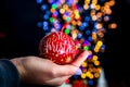 Holding Merry Christmas bauble decoration isolated on background with blurred lights. December season, Christmas composition Royalty Free Stock Photo