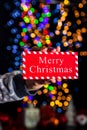 Holding Merry Christmas sign isolated on background with blurred lights. December season, Christmas composition Royalty Free Stock Photo