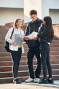 Holding notepads in hands. Three young students are outside the university outdoors